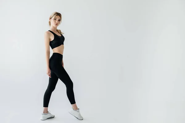 Seitenansicht der jungen blonden Sportlerin in schwarzer Sportbekleidung posiert isoliert auf grau — Stockfoto