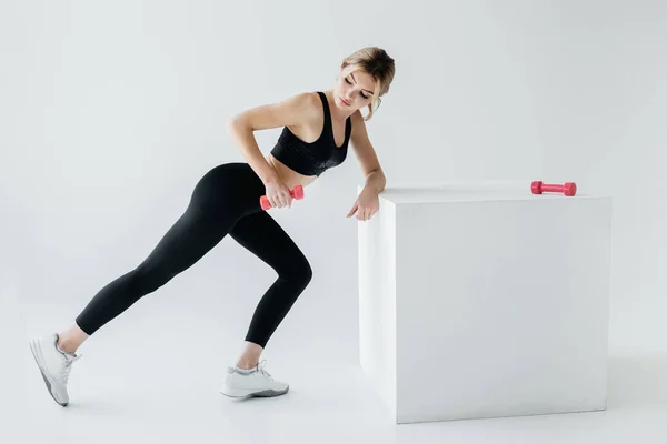 Vue latérale d'une jolie femme en tenue de sport noire s'exerçant avec des haltères sur fond gris — Photo de stock