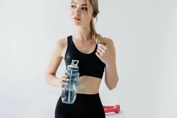 Portrait of athletic woman in black sportswear with sportive water bottle on grey backdrop — Stock Photo