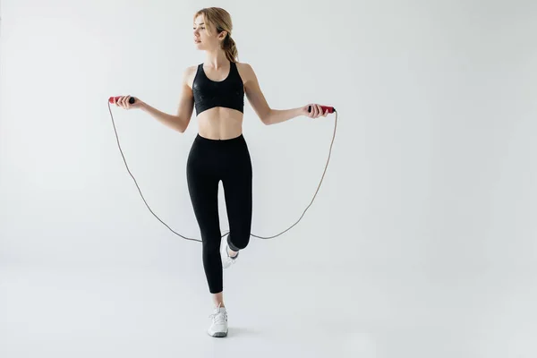 Jeune femme sportive faisant de l'exercice avec corde à sauter isolée sur gris — Photo de stock