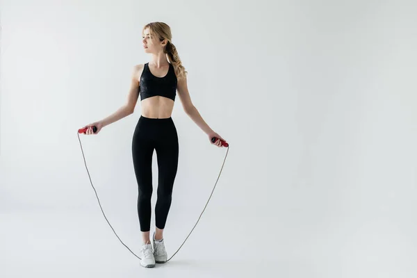 Jovem mulher esportiva com pular corda isolada no cinza — Fotografia de Stock