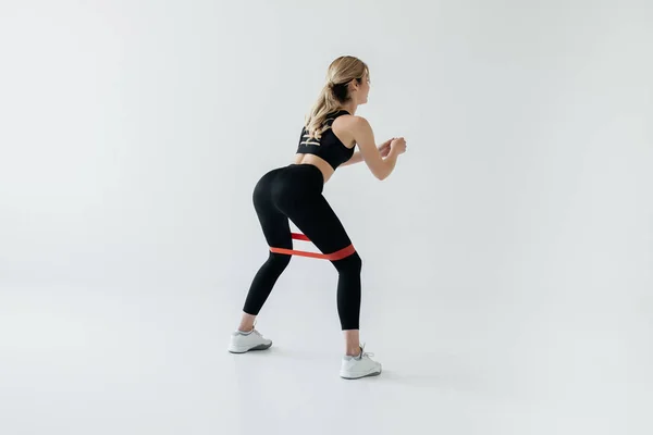 Young athletic sportswoman exercising with rubber tape isolated on grey — Stock Photo
