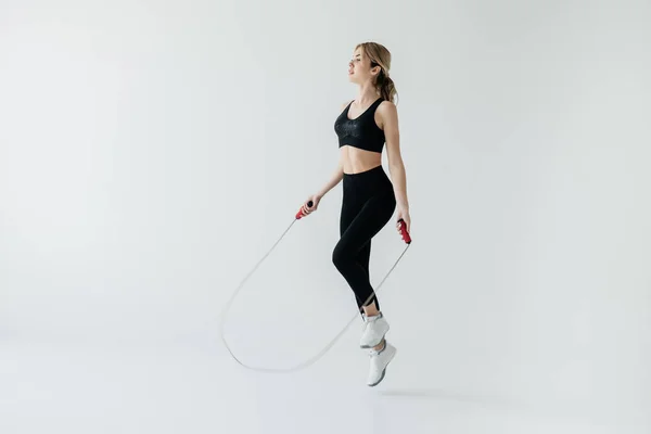 Jovem mulher esportiva exercitando com pular corda isolada no cinza — Fotografia de Stock