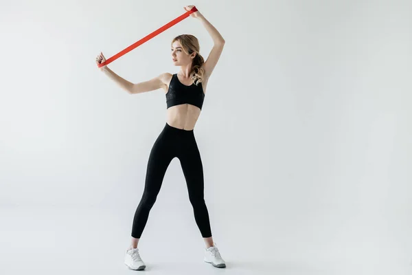 Young athletic woman exercising with rubber tape isolated on grey — Stock Photo