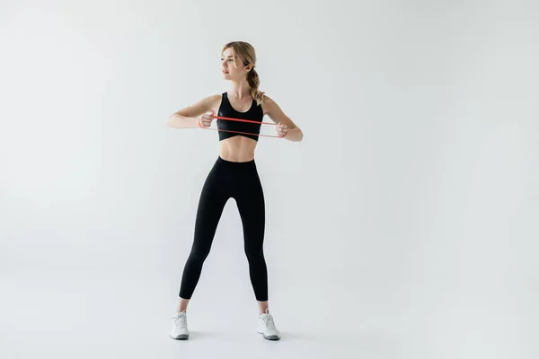 Junge athletische Frau trainiert mit Gummiband isoliert auf grau — Stockfoto