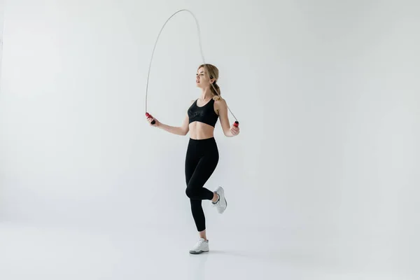 Молодая спортивная женщина упражняется с скакалкой изолированы на сером — стоковое фото