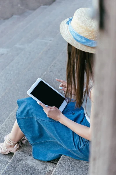 Enfoque selectivo de la chica en el sombrero sentado en las escaleras y el uso de la tableta digital con pantalla en blanco - foto de stock