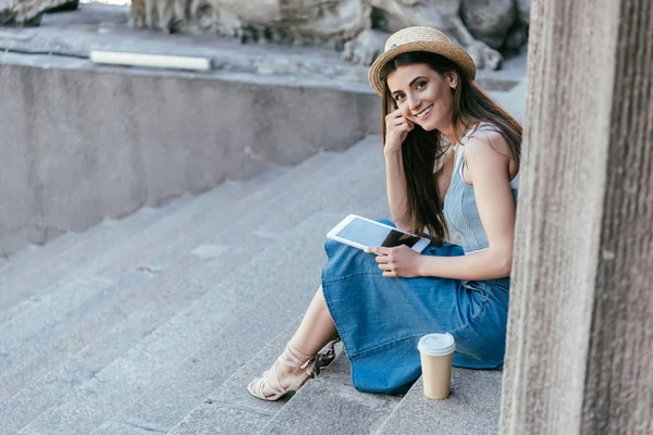 Щаслива молода жінка тримає цифровий планшет і посміхається на камеру, сидячи на сходах — стокове фото