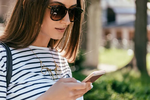 Крупним планом красива дівчина в сонцезахисних окулярах, використовуючи смартфон на вулиці — стокове фото
