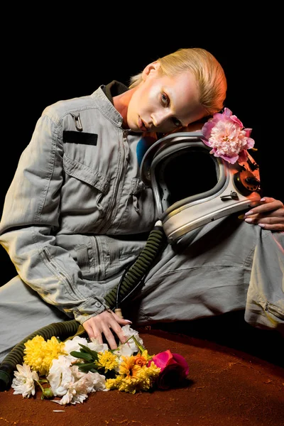 Kaukasischer Astronaut im Raumanzug mit Blumen und Helm sitzt auf dem Planeten — Stockfoto