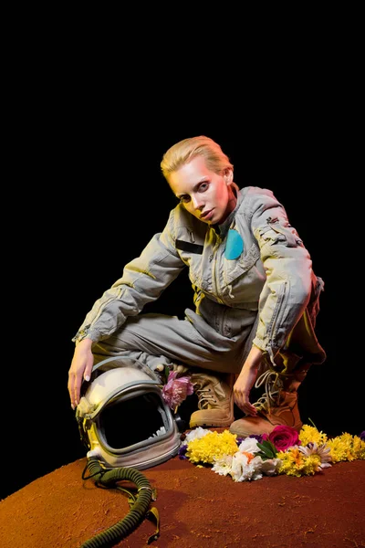 Cosmonauta elegante em trajes espaciais com flores e capacete sentado no planeta — Fotografia de Stock