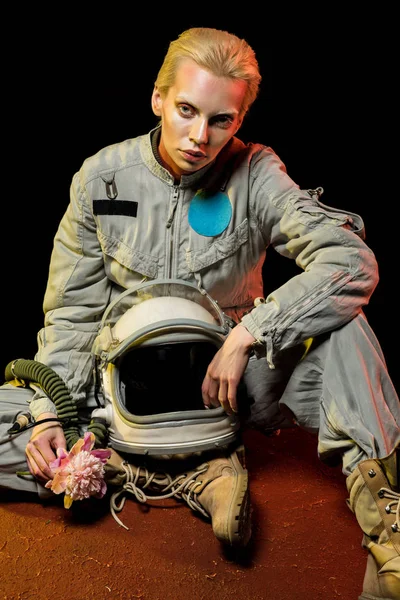 Beautiful spacewoman in spacesuit with helmet and flower sitting on planet — Stock Photo