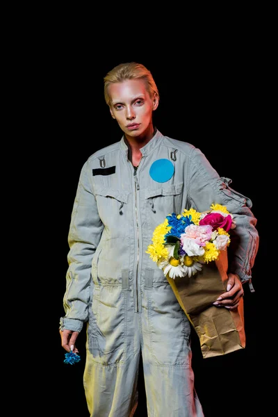 Bel astronaute en combinaison spatiale avec des fleurs dans un sac en papier, isolé sur noir — Photo de stock