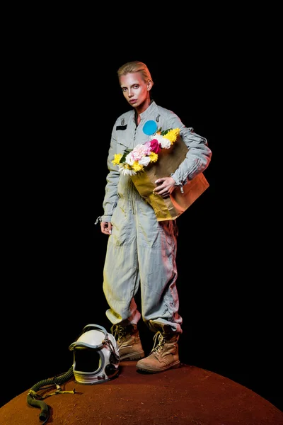 Atractiva astronauta hembra en traje espacial con casco y flores en bolsa de papel de pie sobre marte - foto de stock