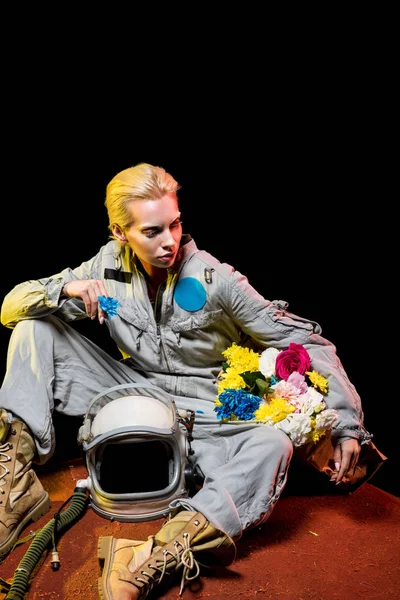 Spacewoman in spacesuit with helmet and flowers in paper bag sitting on red planet — Stock Photo