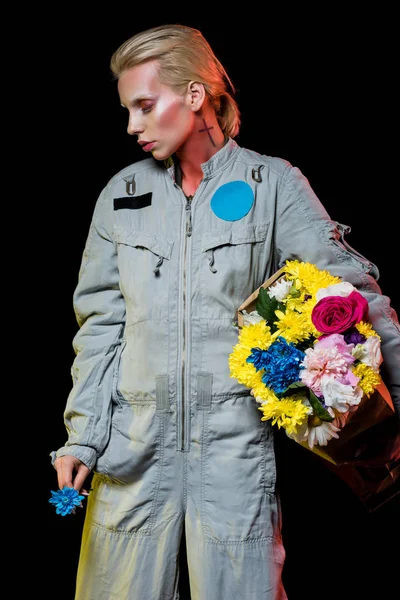 Attrayant astronaute femelle posant en combinaison spatiale avec des fleurs colorées dans un sac en papier, isolé sur noir — Photo de stock