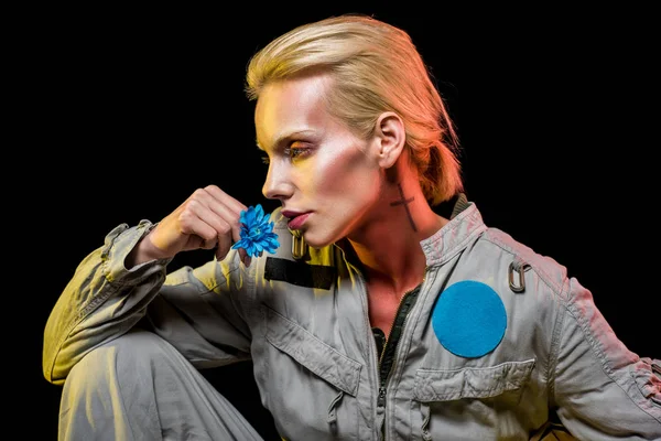 Hermosa cosmonauta femenina posando en traje espacial con flor azul, aislado en negro - foto de stock