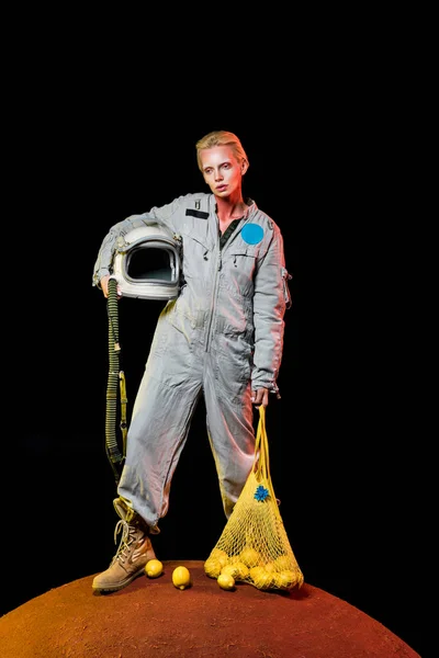 Attractive cosmonaut in spacesuit with helmet and lemons in string bag posing on mars — Stock Photo