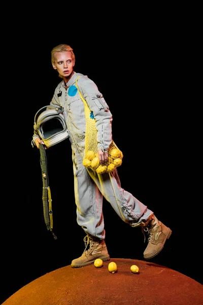 Attractive female astronaut in spacesuit holding helmet and lemons on red planet — Stock Photo