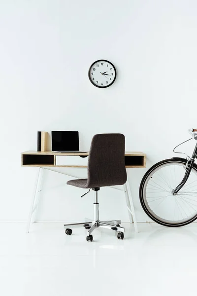 Lieu de travail moderne avec ordinateur portable et vélo devant le mur blanc — Photo de stock