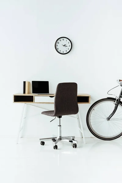 Modern workplace with laptop and bicycle in front of white wall — Stock Photo