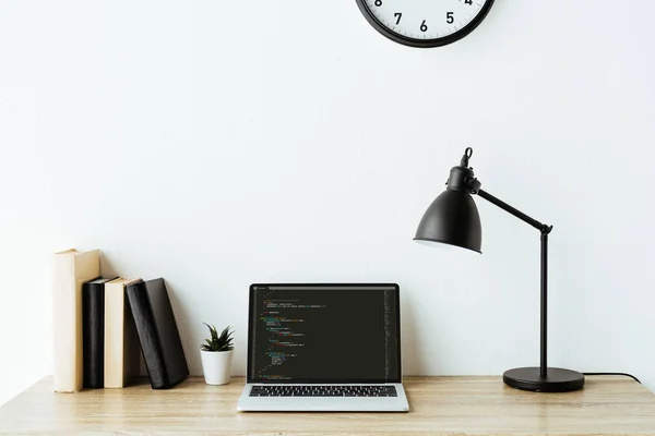 Laptop with program code and books on work desk at office — Stock Photo