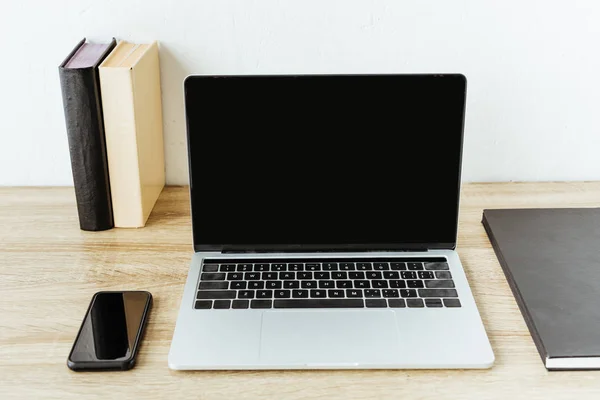 Portátil con smartphone y libros en la mesa de trabajo en la oficina - foto de stock