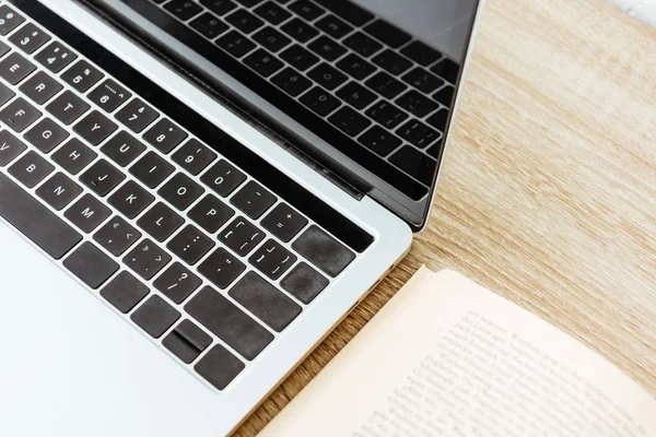 Close-up shot of laptop with opened book on wooden surface — Stock Photo