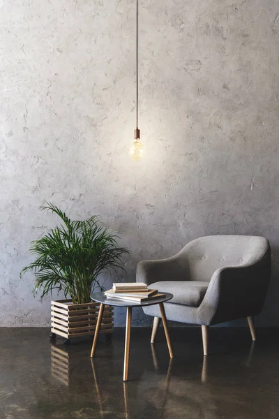 Intérieur de la chambre moderne avec ampoule suspendue, table avec livres, plantes et fauteuils — Photo de stock