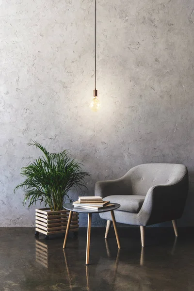 Interior de la habitación moderna con bombilla colgante, mesa con libros, planta y sillón - foto de stock