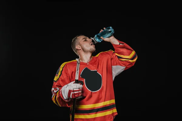 Молодий хокеїст п'є воду зі спортивної пляшки ізольовано на чорному — стокове фото