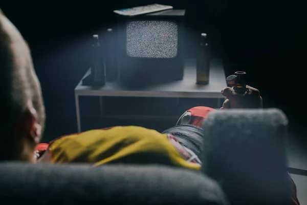 Обрезанный снимок хоккеиста, пьющего пиво и смотрящего телевизор со статическим экраном на черном — стоковое фото