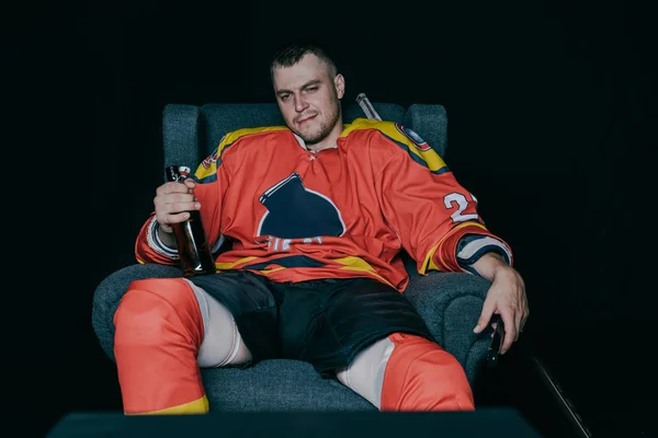 Professional hockey player drinking beer and watching tv on black — Stock Photo