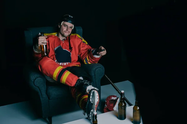 Eishockeyspieler trinkt Bier und schaut Fernsehen auf schwarz — Stockfoto