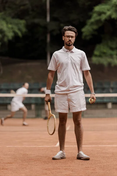 Jugador de tenis de estilo retro de pie con raqueta y pelota en la cancha - foto de stock