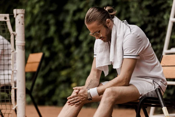 Уставший красивый теннисист сидит на стуле на теннисном корте — стоковое фото