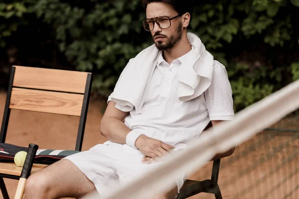 Ernst gut aussehender Tennisspieler ruht sich auf Stuhl am Tennisplatz aus — Stockfoto