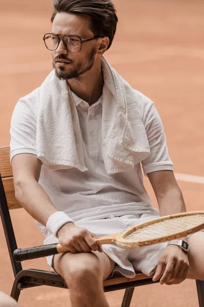 Schöner Tennisspieler sitzt auf Stuhl mit Tennisschläger auf dem Platz — Stockfoto