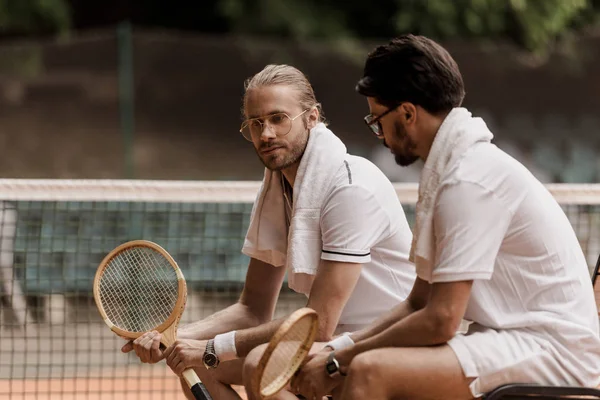 Тенісисти в стилі ретро сидять на стільцях з рушниками і ракетками на тенісному корті — стокове фото