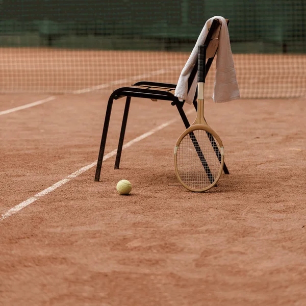 Silla con toalla y raqueta de tenis con pelota de tenis en la pista - foto de stock