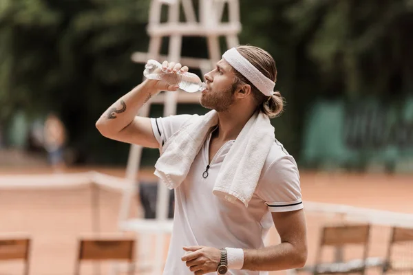 Vista lateral del guapo jugador de tenis de estilo retro beber agua en la cancha de tenis - foto de stock