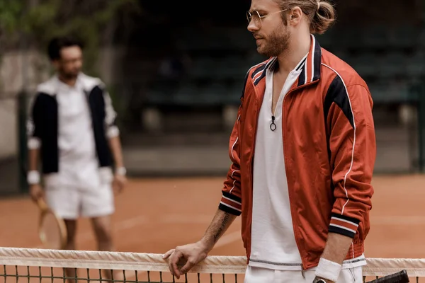 Jugador de tenis de estilo retro apoyado en la red de tenis durante el juego en la cancha de tenis - foto de stock