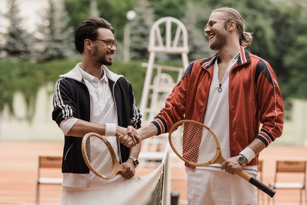 Felices jugadores de tenis de estilo retro estrechando la mano en la cancha de tenis - foto de stock