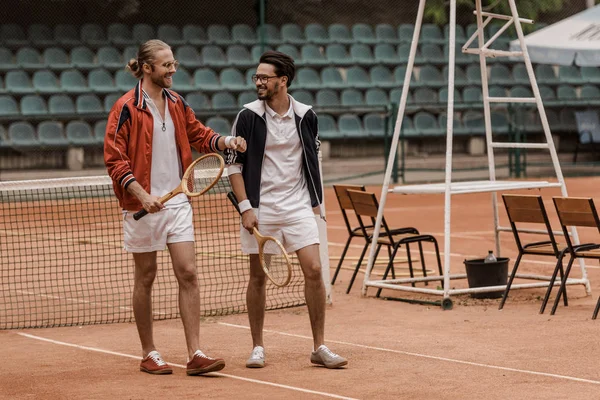 Smiling handsome tennis players walking and looking at each other at court — Stock Photo