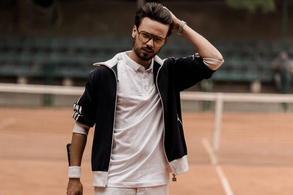 Handsome tennis player touching hair and looking at camera at tennis court — Stock Photo