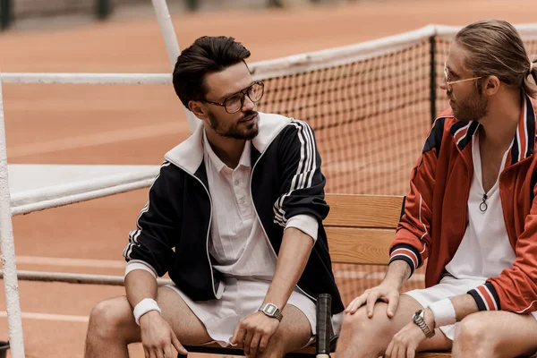 Retro styled tennis players sitting on chairs at tennis court and looking at each other — Stock Photo