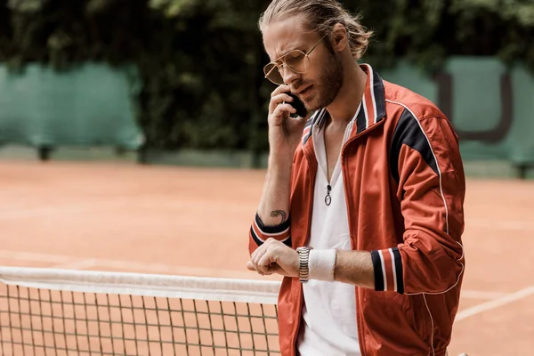 Retro gestylte Tennisspielerin spricht auf Tennisplatz per Smartphone und checkt Uhrzeit — Stockfoto