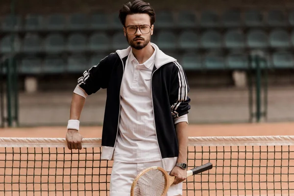 Schöner Tennisspieler, der auf dem Tennisplatz in die Kamera schaut und einen Schläger hält — Stockfoto