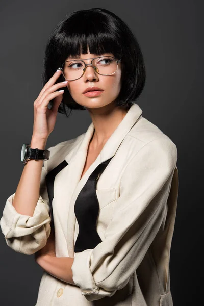 Atractiva joven en chaqueta elegante y gafas mirando hacia otro lado aislado en gris - foto de stock