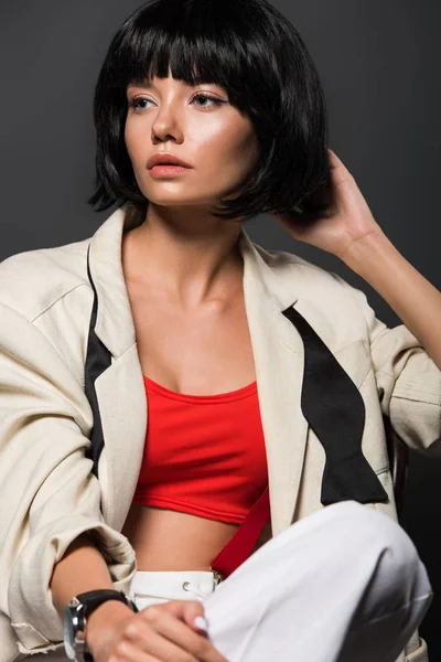 Hermosa mujer joven en chaqueta elegante mirando hacia otro lado aislado en gris - foto de stock